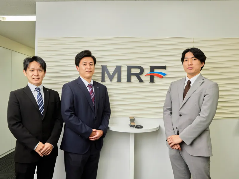 MRFのロゴの前に並ぶ社員たち